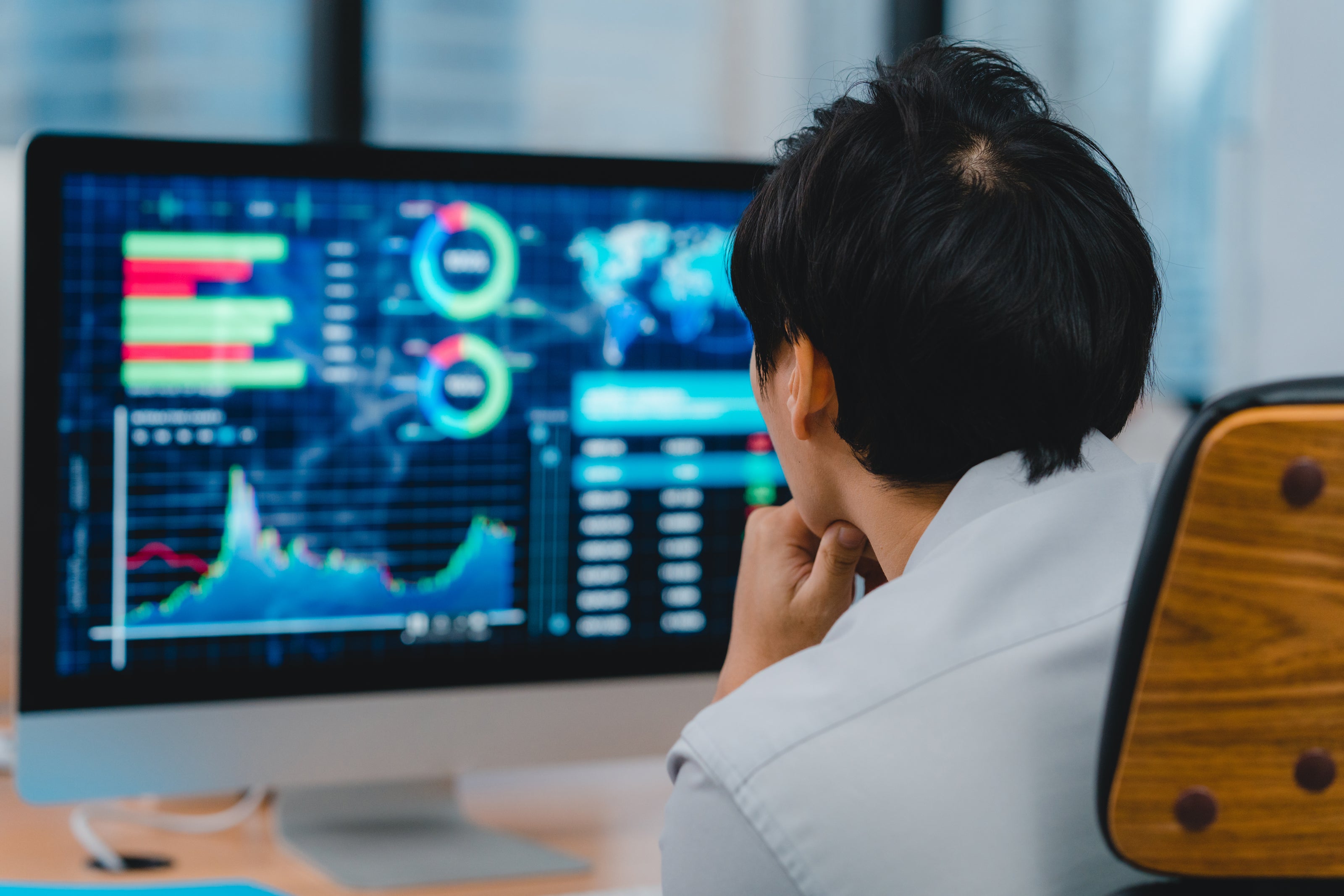 Person sitting in front of a computer monitor with financial charts on a desk.