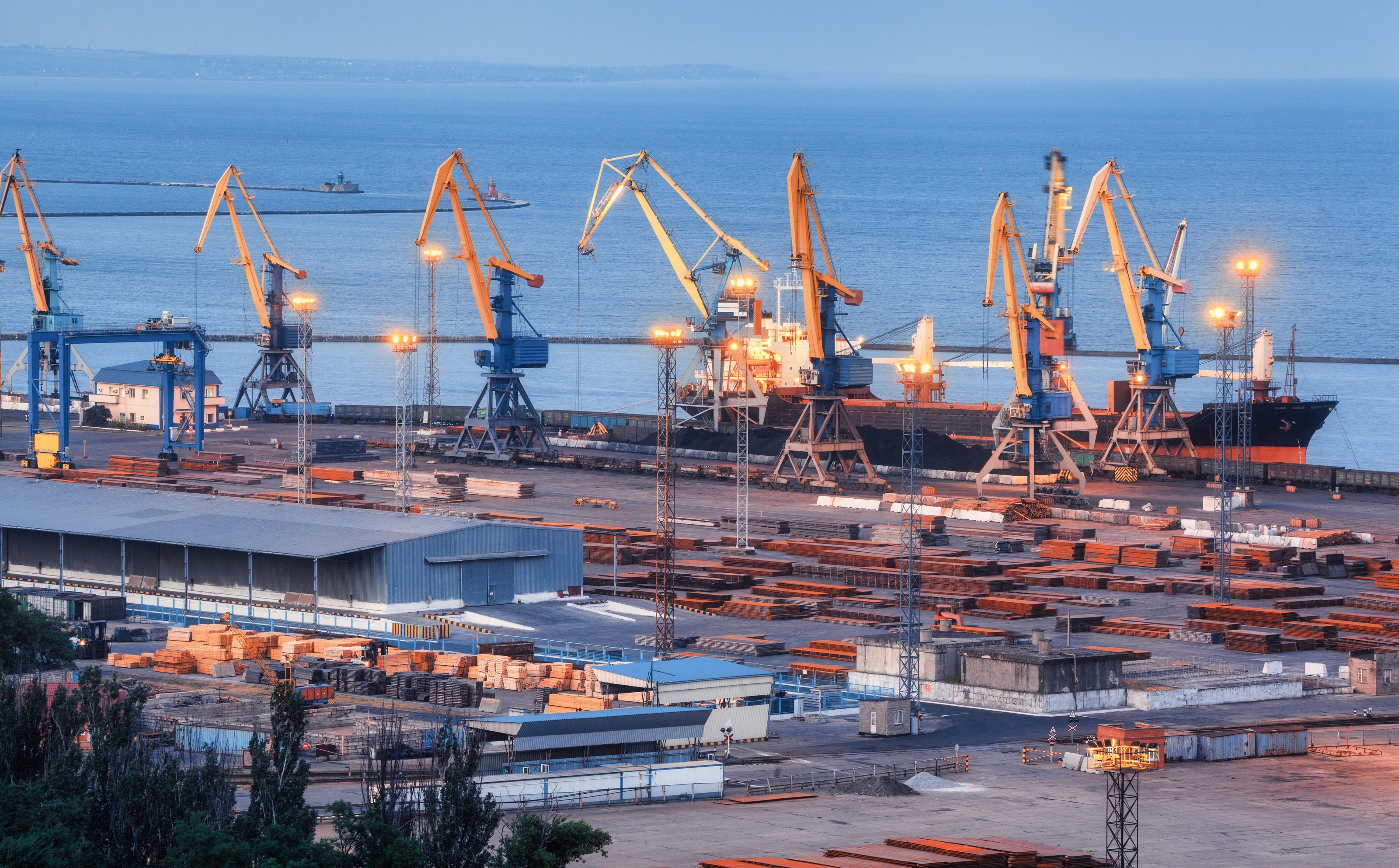 Industrial port scene with cranes and shipping containers at dusk.